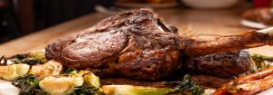 A tomahawk steak served with brussel sprouts and roasted vegetables